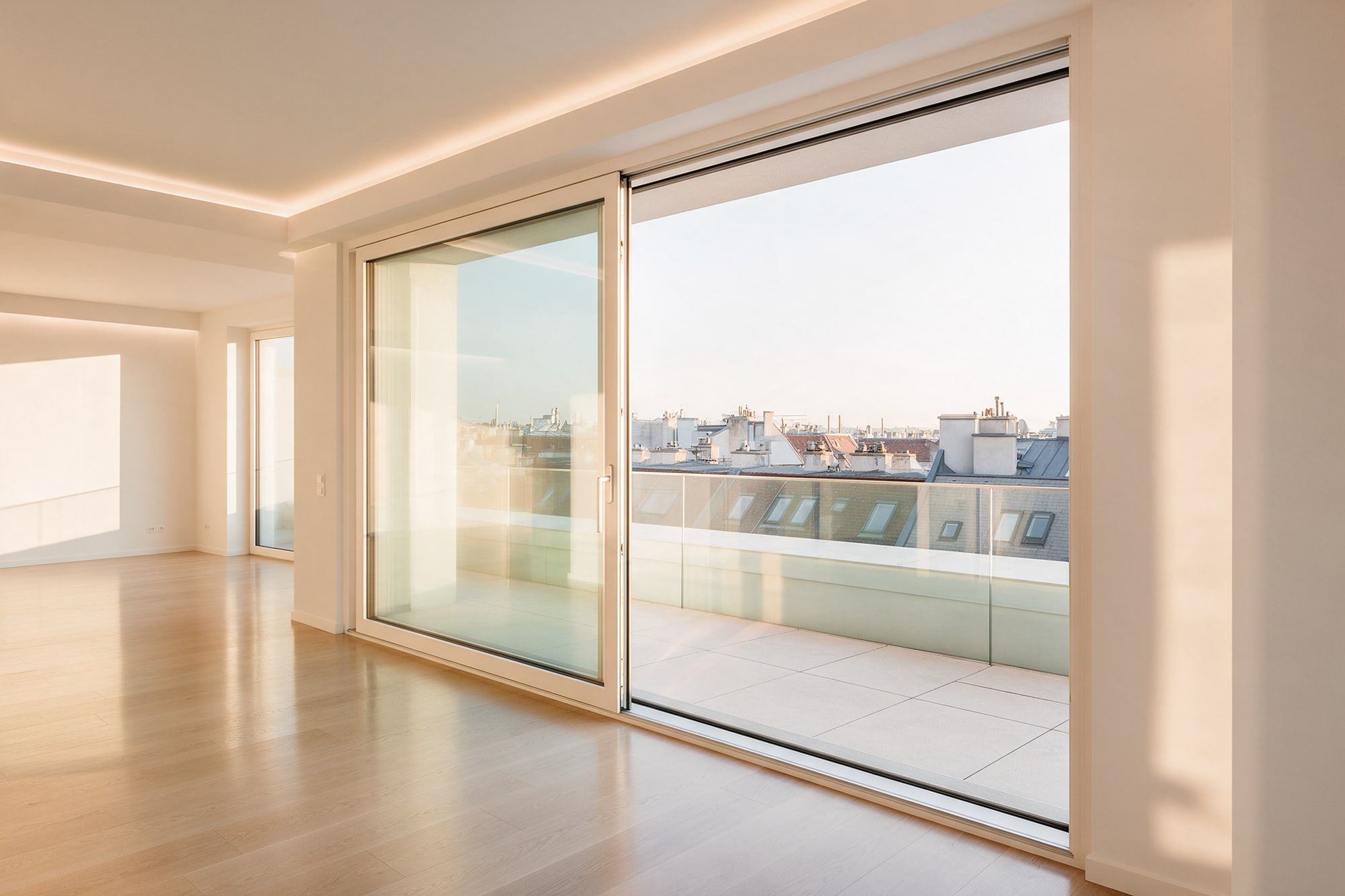Glasschiebetür zu einer Terrasse mit Glasgeländer über den Dächern der Stadt